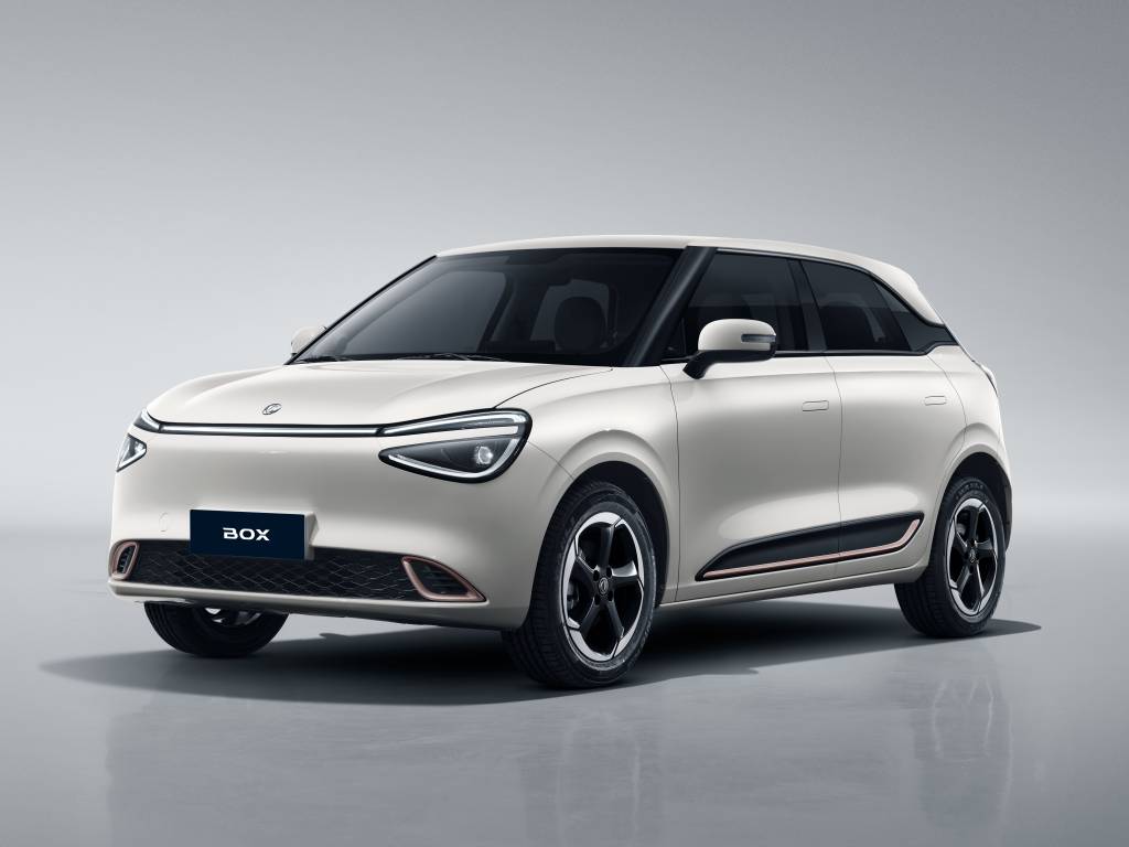 Carro elétrico branco, modelo Box, com detalhes em preto e laranja na lateral, parado em um estúdio com fundo cinza claro