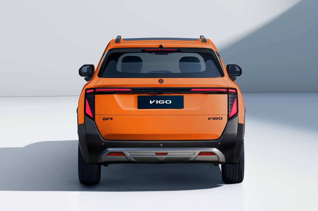 Traseira de um carro laranja VIGO, com detalhes em preto fosco e um para-choque prateado. As lanternas verticais têm luzes vermelhas acesas, e o nome VIGO aparece na placa e no canto inferior direito da tampa do porta-malas. O veículo está em um estúdio branco com sombras suaves