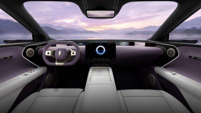Interior de um carro moderno com painel e volante em tons de roxo e cinza claro. O painel possui uma tela central exibindo um círculo branco brilhante. O para-brisa revela uma paisagem montanhosa com céu roxo e nuvens ao pôr do sol