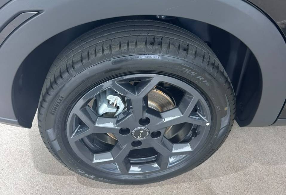 Pneu Pirelli preto com aro escuro de cinco pontas duplas, freio a disco e pinça prateada, sob o para-lama cinza de um carro